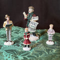Miniature Christmas figurines including Christmas carolers and newspaper seller