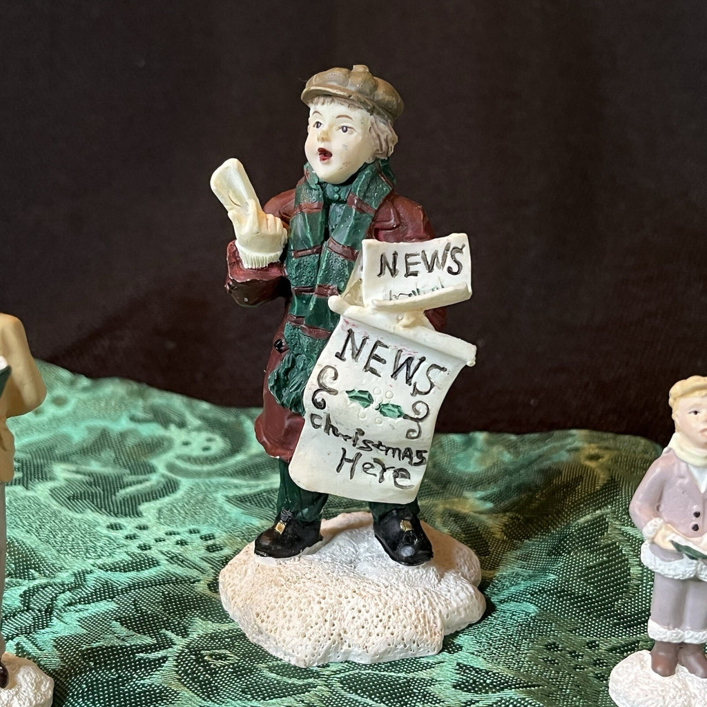 Miniature Christmas figurines including Christmas carolers and newspaper seller